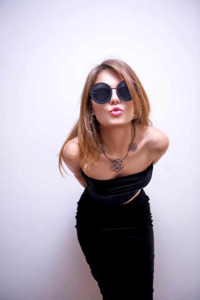 Blonde Haired Woman In Round Black Sunglasses Pouting Behind White Concrete Wall