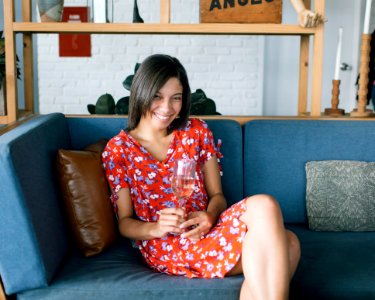 Woman Sitting At Sofa Wearing Red And Multicolored Floral Dress White Holding Glass photo
