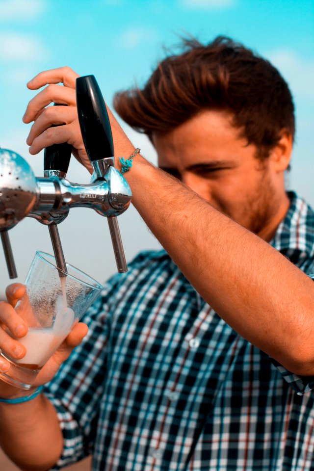 Man Holding Black Beer Tap Handle Pouring Beer On Clear Glass photo