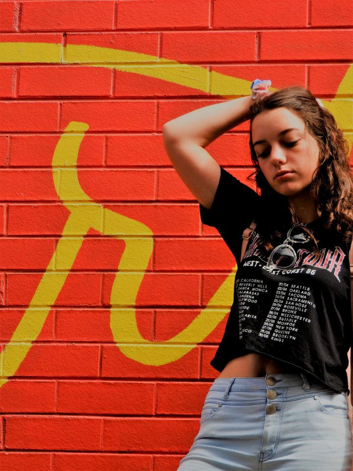 Woman In Black Shirt And Blue Bottoms Standing Near Red Wall