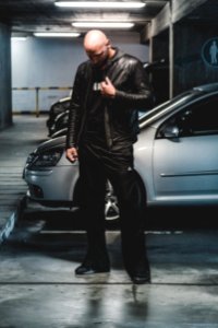 Man In Black Leather Jacket Standing In Front Of Gray Car photo