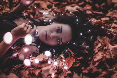 Woman Lying On Dried Leaves Holding String Lights