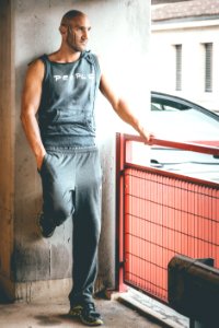 Man Wearing Gray Tank Top And Track Pants Leaning On Wall photo