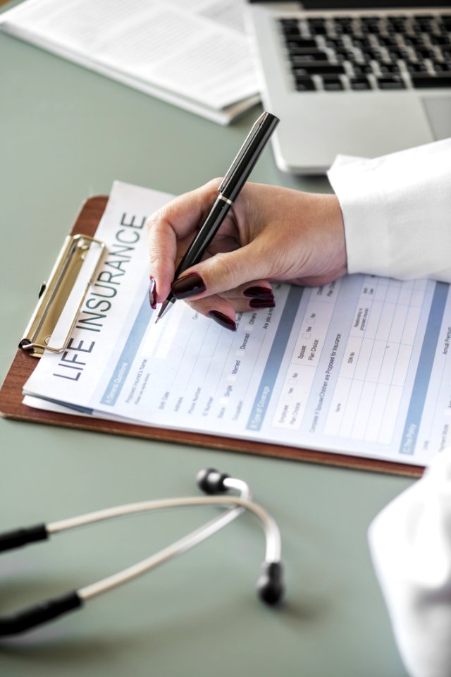 Person Holding Pen Writing On Life Insurance Paper