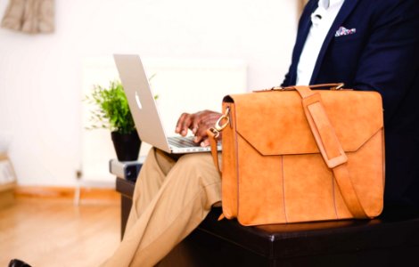 Person Wearing Blue Suit Beside Crossbody Bag And Using Macbook photo