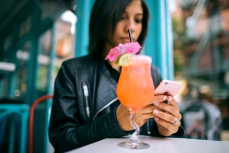 Woman Holding Mobile Phone With A Cocktail Glass On The Table