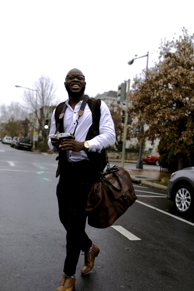 Man In White Button-up Dress Shirt Holding Camera While Smiling And Crossing Street