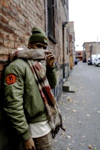 Man Wearing Bubble Jacket With Scarf Leaning On Wall