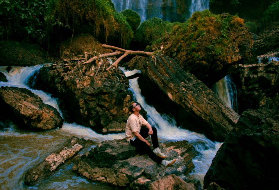 Photo Of Man Sitting On Gray Rock Surrounded By Water Falls