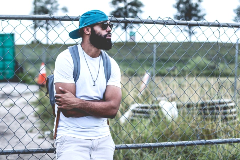 Selective Focus Photography Of Man In White Crew-neck T-shirt Leaning On Gray Metal Chain Fence photo