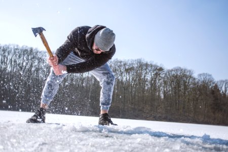 Man Wearing Black Hooded Jacket Gray Knit Cap Gray Pants And Black Shoes Holding Brown Handled Axe While Bending On Snow photo