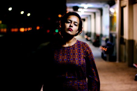 Woman In Brown And Purple Long-sleeved Shirt Standing Outside White Building During Nighttime photo