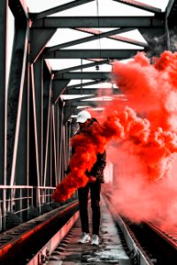 Man In Black Jacket Holding Red Smoke On Metal Bridge