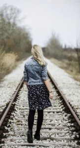 Woman In Blue Denim Jacket Black Leggings And Black And White Dress Walking On Train Rail