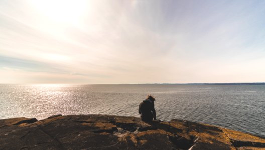 Person Sitting On Stone In Front Of Sea Water