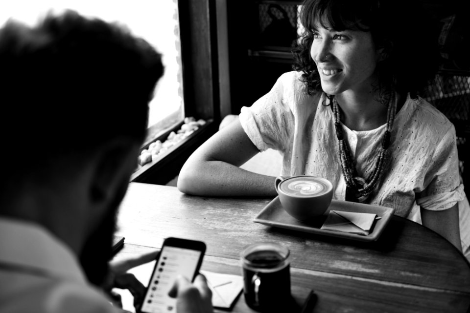 Grayscale Photography Of Man And Woman Sitting Beside Wooden Table