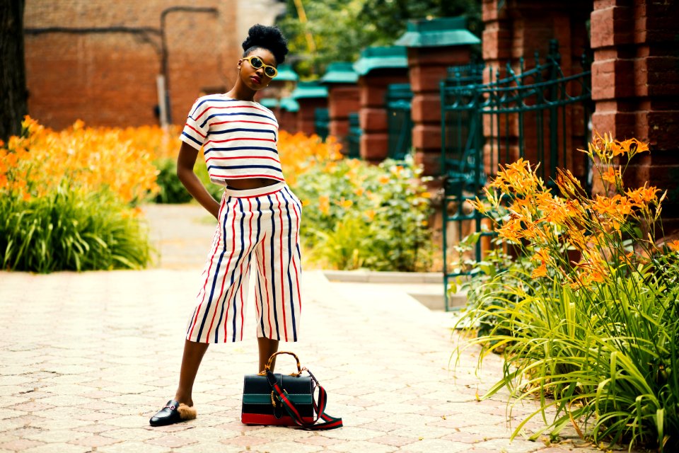 Woman Wearing White Black And Red Striped Crew-neck T-shirt With Matching Pants Standing Outside Beside Black Leather 2-way Bag