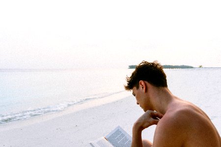 Topless Man Reading Book While Seating At Beach