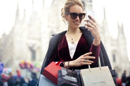 Woman In Maroon Long-sleeved Top Holding Smartphone With Shopping Bags At Daytime photo