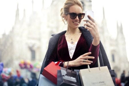 Woman In Maroon Long-sleeved Top Holding Smartphone With Shopping Bags At Daytime