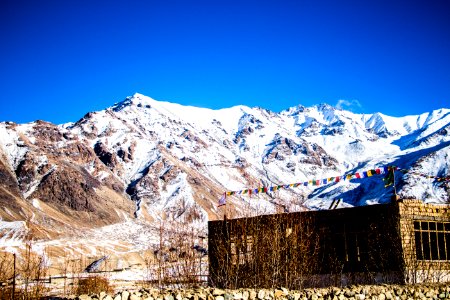 Stone Building At The Base Of Snow-covered Mountain Range Under Clear Bright Blue Sky