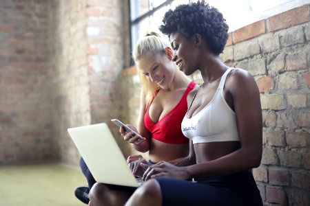 Two Women Wearing Red And White Sports Bras Sitting Near Brown Wall Bricks