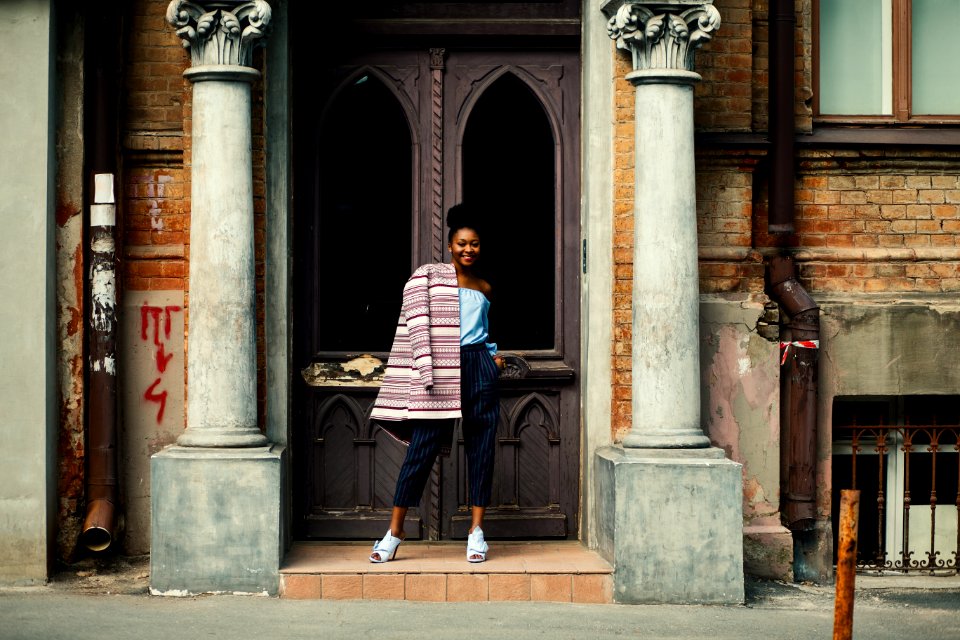 Woman In Blue Strapless Top And Black Pants Standing Next To Brown Wooden Door