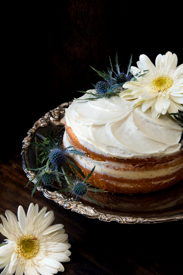 Fondant Cake Whipped With White Icing And Topped With White Petaled Flower On Grey Stainless Steel Plate