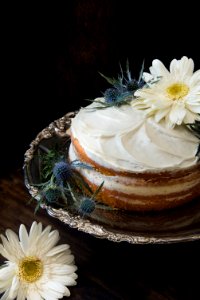 Fondant Cake Whipped With White Icing And Topped With White Petaled Flower On Grey Stainless Steel Plate