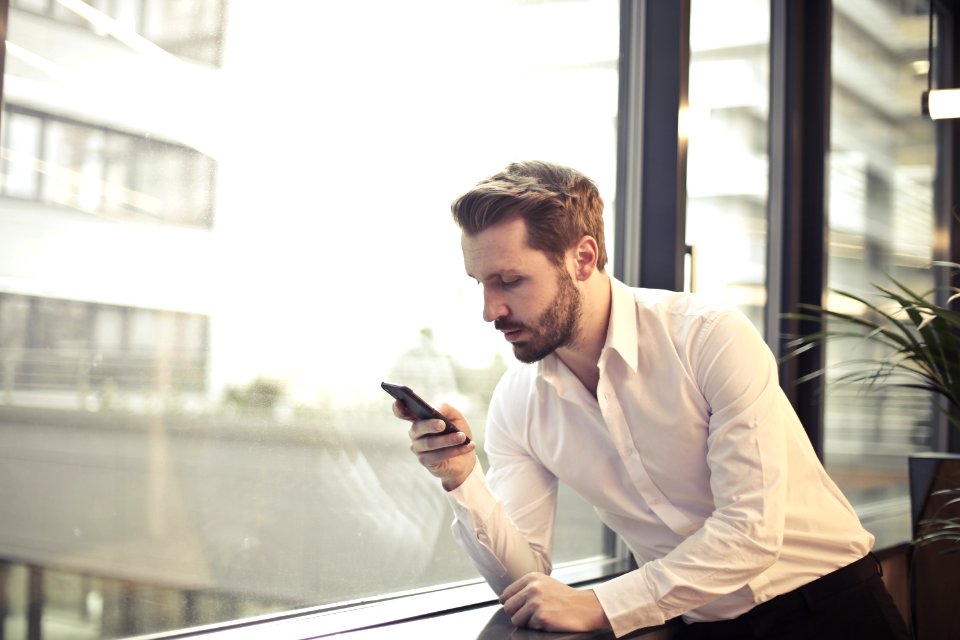 Photo Of Man In White Dress Shirt Holding Phone Near Window photo