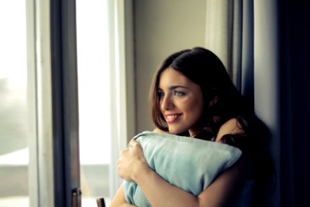 Woman Hugging White Pillow Beside Glass Door photo