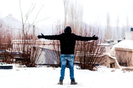 Person Wears Black Jacket And Blue Denim Jeans Standing On Snow Covered Field