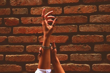 Person Wearing Watch And Rings Raising Left Hand Near Brick Wall