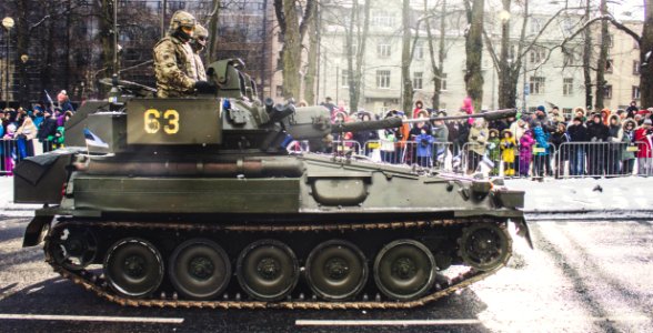 Two Soldiers Ride On Green Military Tank Surrounded With People