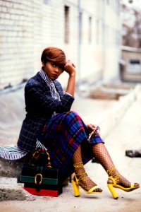 Woman Wearing Black And Grey Tattersall Blazer And Multicolored Plaid Skirt With Black Mesh Stocking And Yellow Chunky Heeled Sand