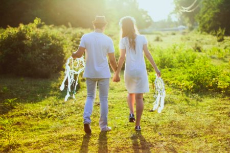 Coupe With White Dress And Suit Holding A White Dreamcatcher While Walking On Green Grass