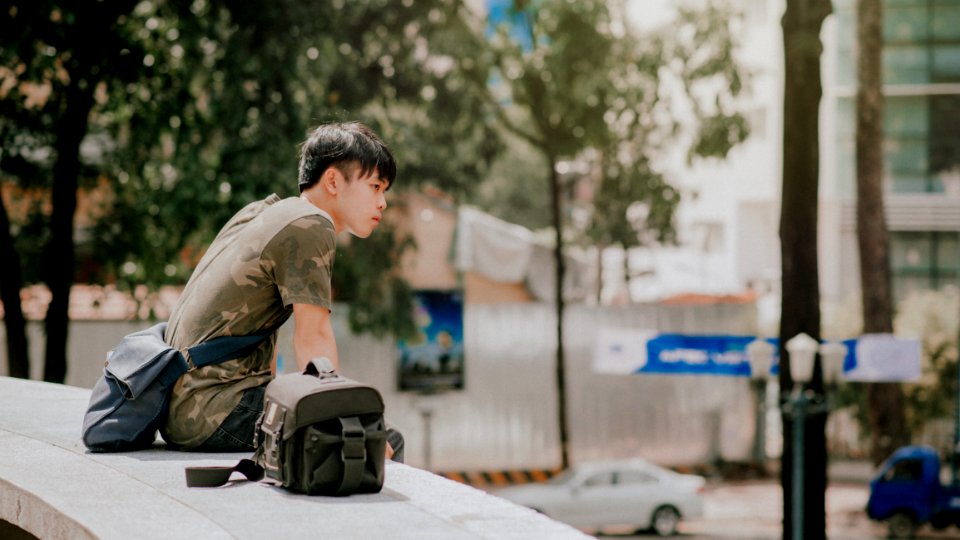 Man In Green And Beige Camouflage T-shirt Siting Beside Bag At Daytime