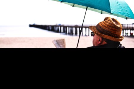 Man Sitting On Chair Under Blue Umbrella Near Beach