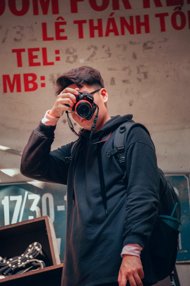 Man Holding Camera Beside Text Printed Wall
