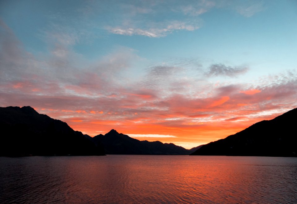 Body Of Water Near Silhouette Of Mountain Under White Clouds During Sunset