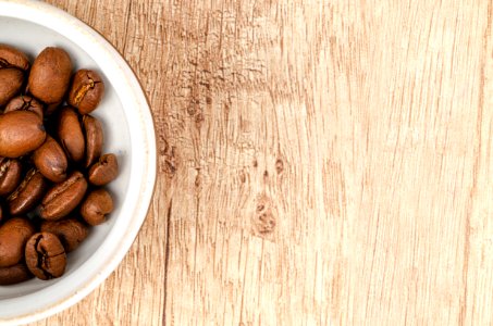 Coffee Beans On White Ceramic Bowl On Top Of Brown Wooden Surface