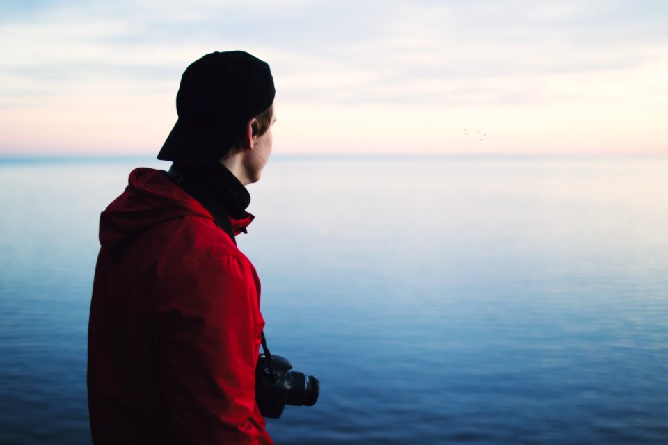 Man In Red Jacket Standing Near Body Of Water
