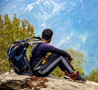 Man In Purple T-shirt With Blue Backpack Sitting On Gray Boulder photo