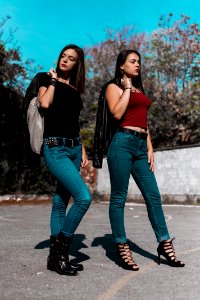 Woman In Black Cap-sleeved Shirt And Blue Denim Jeans Beside Woman In Red Spaghetti Strap Shirt Holding Black Leather Jacket At Da