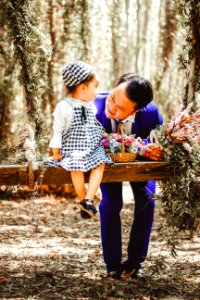 Selective Focus And Color Photography Of Man Looking At Her Girl Sitting On Garden Swing White Holding Bouquet Of Flower In Brown