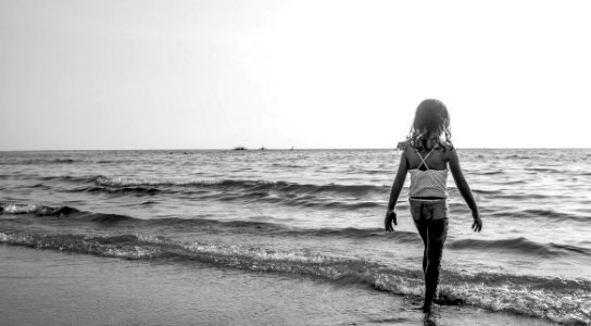 Grayscale Photo Of Girl Walking On Seashore With White Spaghetti Strap Top