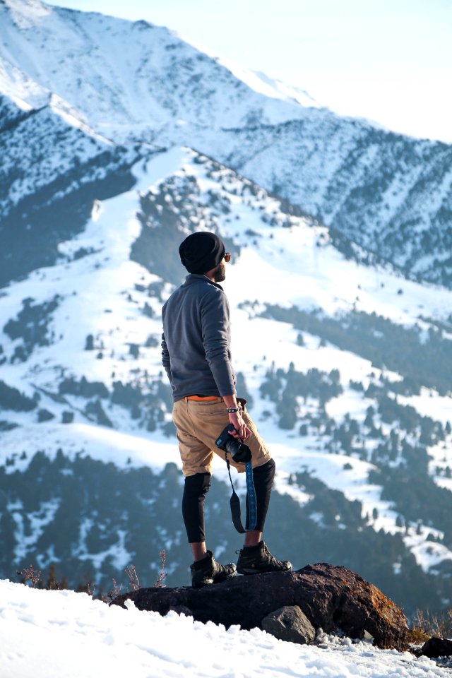 Man Wearing Gray Long-sleeved Shirt And Brown Shorts Holding Black Dslr Camera On Mountain