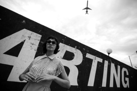 Grayscale Photo Of Woman Standing Beside Wall