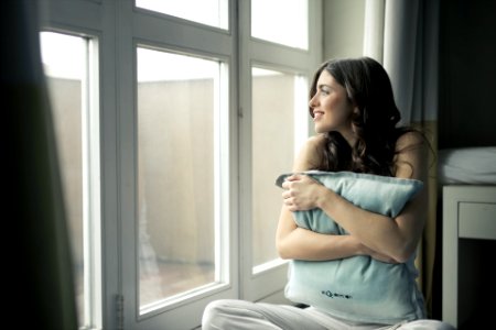 Black Haired Woman Hugging Gray Pillow Near Glass-panel Window