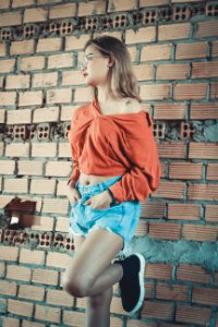 Woman Wearing Brown Long-sleeved Blouse And Blue Denim Short Shorts Standing Behind Brown Brick Wall photo